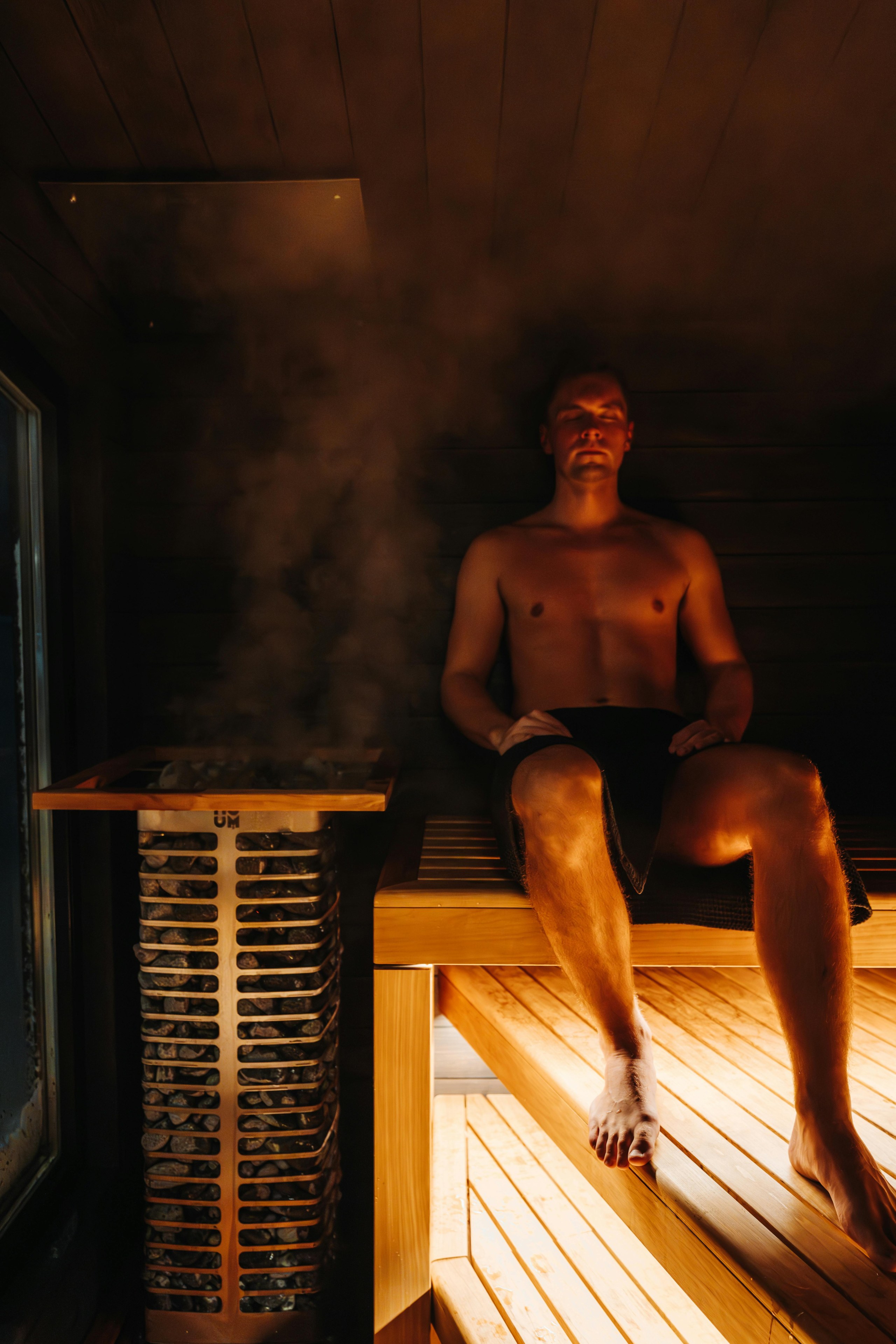 Een man zit in een sauna bij een dampende saunakachel.