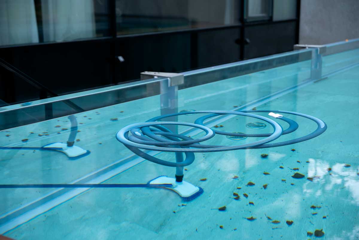 Een schoonmaakbezem ondergedompeld in het water van een buitenzwembad, voor het reinigen van de bodem en de wanden, als het zwembad vol ligt met bladeren en andere tekenen van verwaarlozing - vuil.