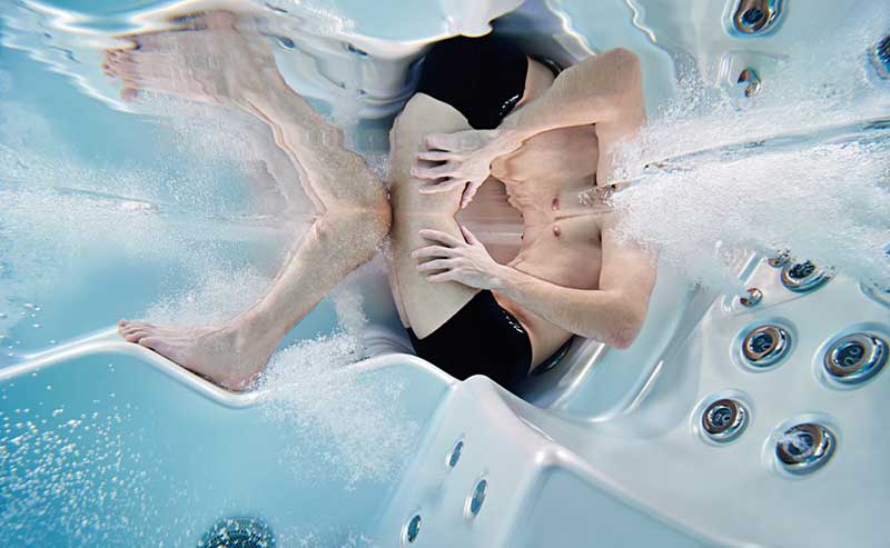 Vrouw ontspant in een ergonomische ligstoel in een USSPA-spabad met werkende hydromassagejets.
