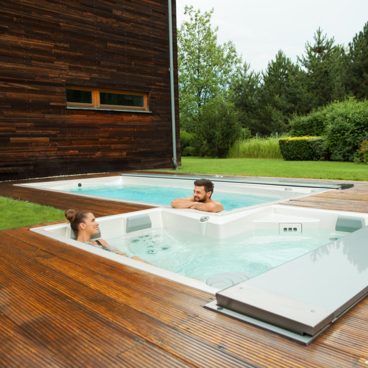 Een stel ontspant in de buitenbaden van USSPA, bestaande uit een spa en een swimspa, die op een houten terras zijn geïnstalleerd.