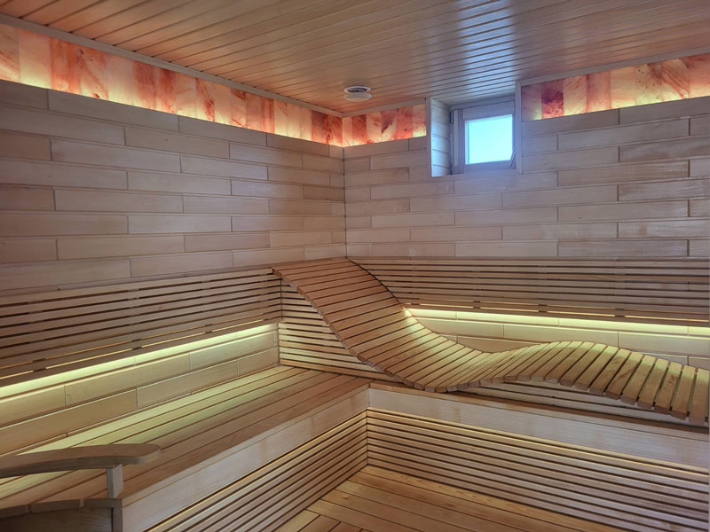Lichte houten sauna met golvende bank en ledverlichting.