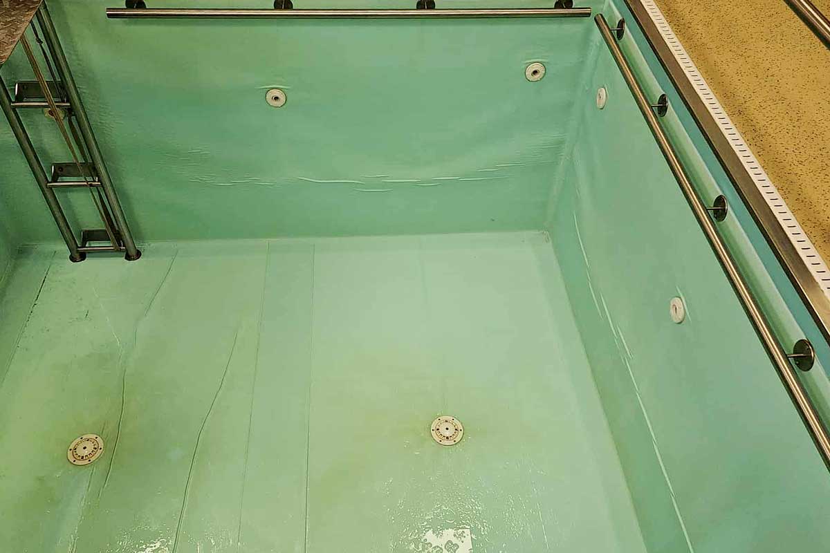 De bodem van het zwembad is bedekt met een laag groene algen, het water is troebel en geeft de indruk van een verwaarloosde, vuile omgeving.
